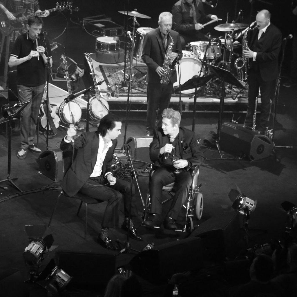 Shane at his 60th birthday concert on stage with Nick Cave – by Andrew Catlin